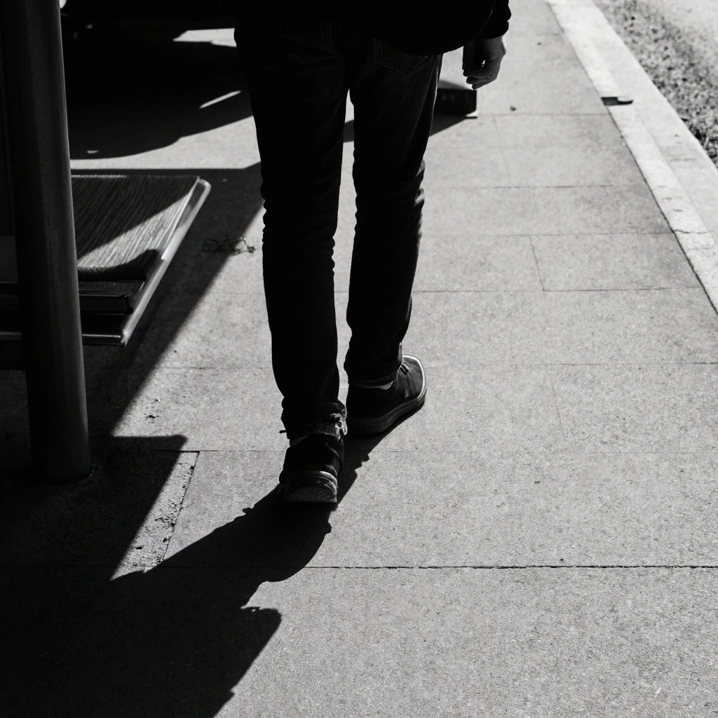 Black and white photography with shadows catching the foot of a stranger meandering around a bus station in a weird world