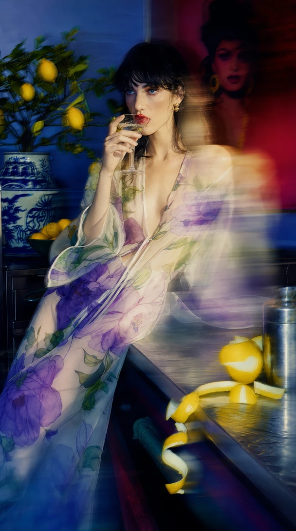 motion blur Fashion photography, portrait of a model with dark hair, red lips, blue eyes drinking martini in a sheer translucent chiffon dress with ov