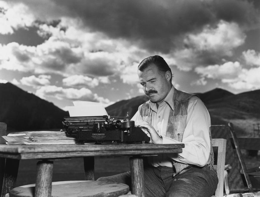 ernest Hemingway writing outdoors in Sun Valley, Idaho, in 1939 while working on For Whom the Bell T…
