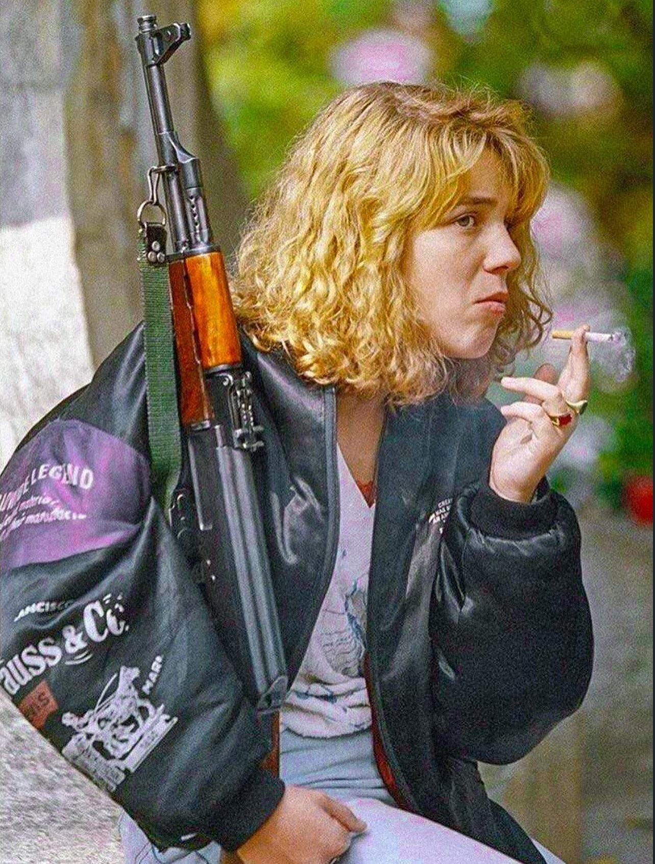 a young Bosnian woman holding an AK-47. Smokes a cigarette as she waits for a funeral service in Sar…