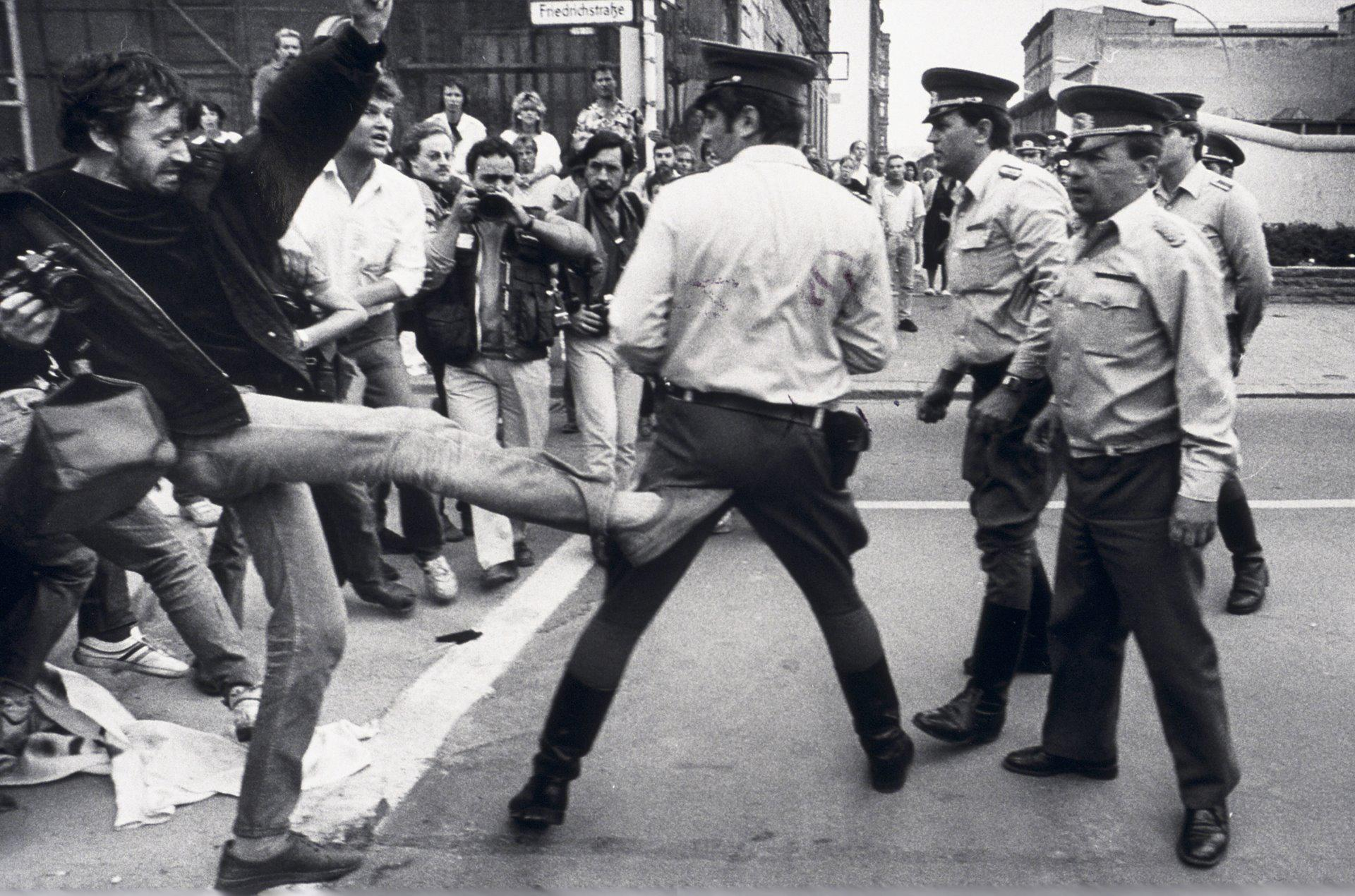 a West Berliner reaching over the border to kick an East German police officer. (1986)